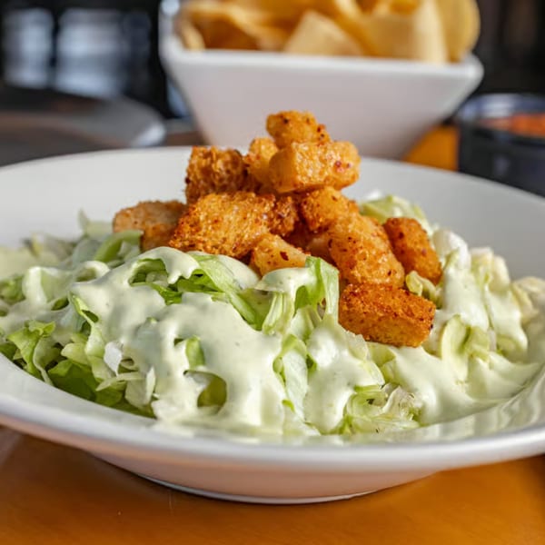 A white bowl of Jefe's Cantina + Cocina's Mexican salad with lettuce, creamy dressing, and crispy croutons.
