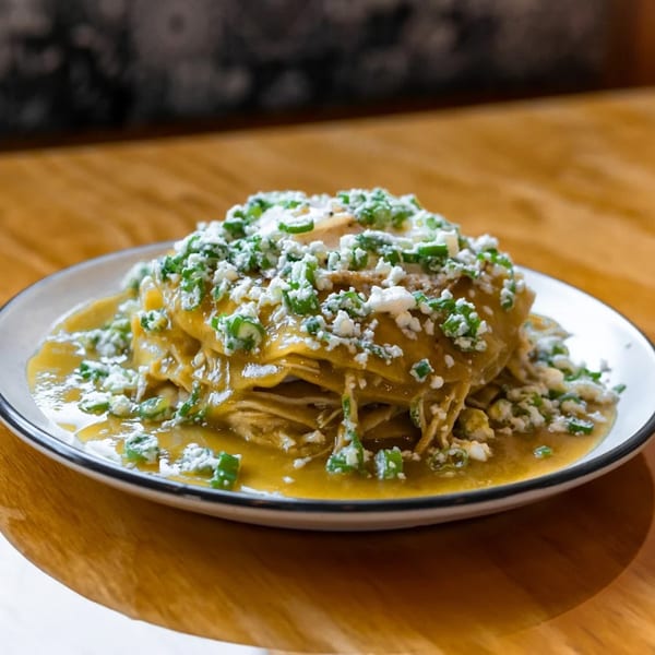 Stacked green enchiladas with shredded chicken, green sauce, crumbled cheese, and green onions.