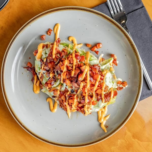 A wedge salad with bacon, tomatoes, and a creamy orange dressing on a gray plate.
