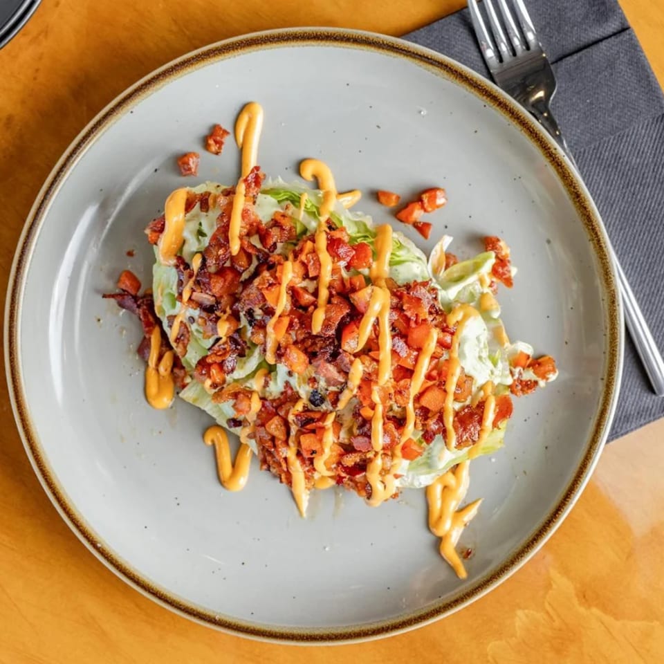 A wedge salad with bacon, tomatoes, and a creamy orange dressing on a gray plate.