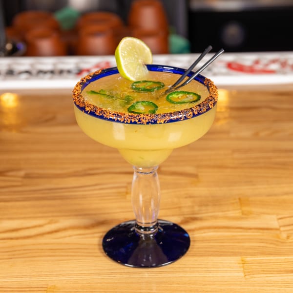 Jefe's Cantina + Cocina's spicy margarita with lime and jalapeño slices on a wooden bar.
