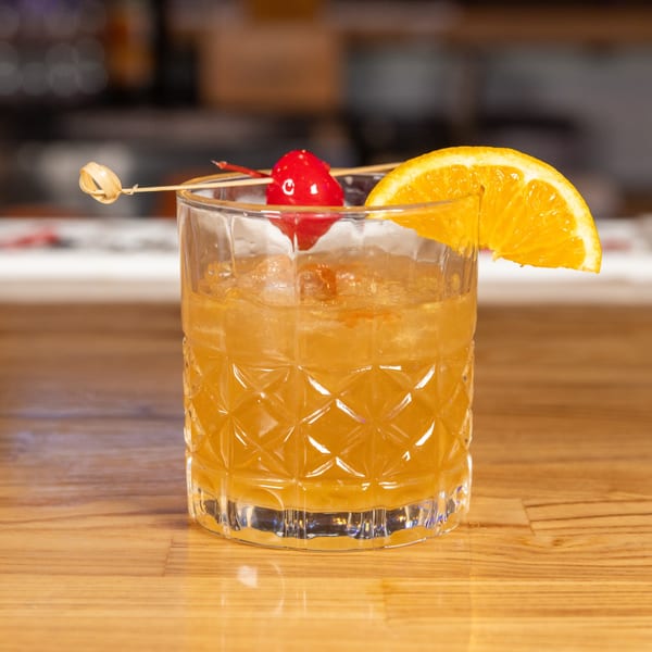 Jefe's Cantina + Cocina's cocktail with an orange slice and cherry on a wooden bar.
