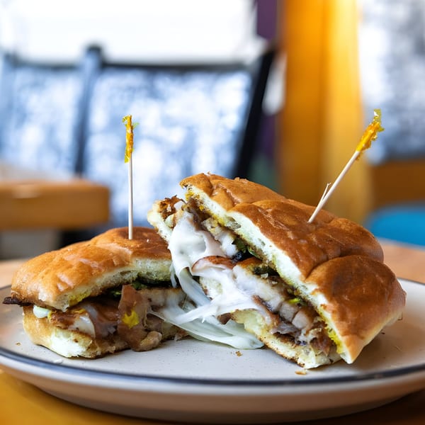 A Mexican torta sandwich, cut in half, revealing melted cheese and meat, on a white plate.